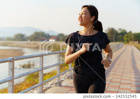 Asian woman jogging on pathway during sunny morning outdoors Asian woman jogging on pathway during sunny morning outdoors 142532545