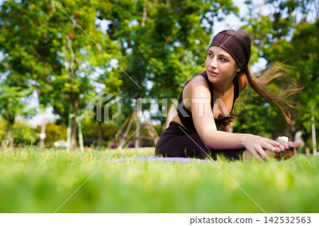 Hispanic woman stretching leg in seated head to knee pose on mat in park Hispanic woman stretching leg in seated head to knee pose on mat in park 142532563