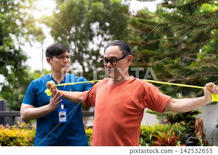 Caregiver helping senior man exercising with resistance band in garden Caregiver helping senior man exercising with resistance band in garden 142532655