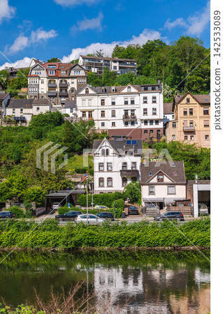 Riverside Houses on Lush Hillside Under Blue Sky Riverside Houses on Lush Hillside Under Blue Sky 142533089