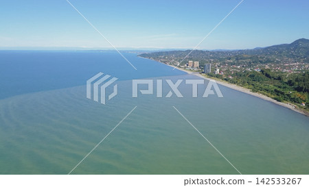 Aerial view of the coastline near Batumi, showcasing the calm sea, sandy beach, and modern buildings along the shore under a clear blue sky Aerial view of the coastline near Batumi, showcasing the calm sea, sandy beach, and modern buildings along the shore under a clear blue sky 142533267