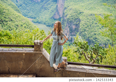 Woman tourist admiring the dramatic Sumidero Canyon viewpoint in Chiapas Mexico with steep canyon walls lush landscape river overlook nature tourism and posing at the observation area. Woman tourist admiring the dramatic Sumidero Canyon viewpoint in Chiapas Mexico with steep canyon walls lush landscape river overlook nature tourism and posing at the observation area. 142533343