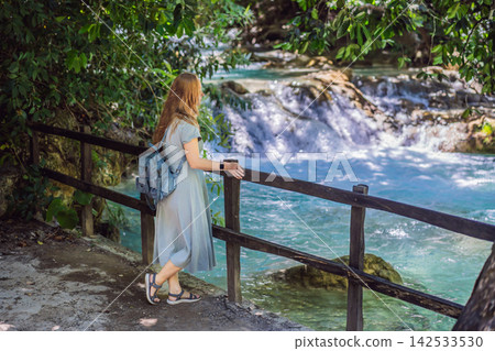 Woman traveler admiring El Chiflon waterfall from a wooden viewpoint in Chiapas Mexico with wooden railings tropical forest clear blue water nature travel and smiling. Woman traveler admiring El Chiflon waterfall from a wooden viewpoint in Chiapas Mexico with wooden railings tropical forest clear blue water nature travel and smiling. 142533530