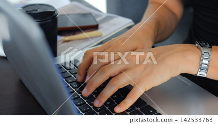 Hands typing on laptop keyboard beside coffee cup notebook and pen on desk in bright office workspace, close view of focused person working on computer for business, communication and remote Hands typing on laptop keyboard beside coffee cup notebook and pen on desk in bright office workspace, close view of focused person working on computer for business, communication and remote 142533763