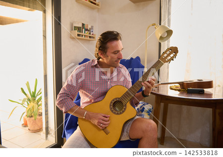 Man playing acoustic guitar at home in a sunlit living room Man playing acoustic guitar at home in a sunlit living room 142533818