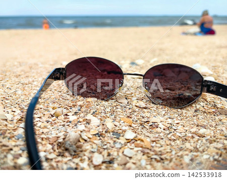 Summer vacation concept featuring sunglasses on a seashell-covered shore. 142533918