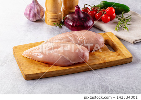 Raw chicken breasts on wooden cutting board with fresh vegetables and herbs 142534001