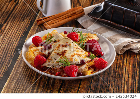 Folded crepes with raspberries and rosemary on rustic wooden table Folded crepes with raspberries and rosemary on rustic wooden table 142534024