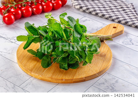 Fresh mint leaves on wooden cutting board with cherry tomatoes and checkered cloth 142534041