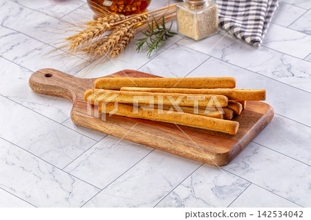 Grissini breadsticks on wooden cutting board with wheat ears and rosemary Grissini breadsticks on wooden cutting board with wheat ears and rosemary 142534042