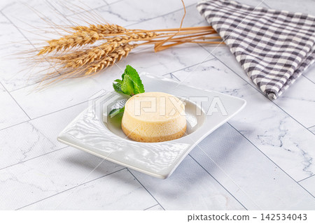 Small cheesecake on white plate with mint garnish and wheat stalks on marble surface Small cheesecake on white plate with mint garnish and wheat stalks on marble surface 142534043