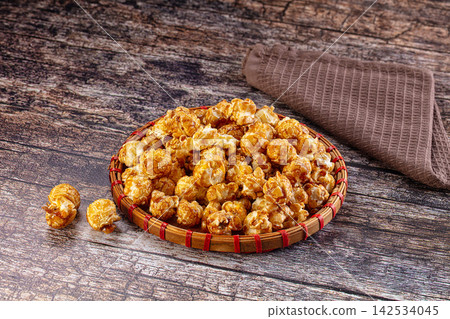 Caramel popcorn in woven basket on rustic wooden table 142534045