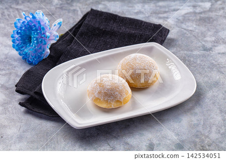 Two mochi desserts dusted with powdered sugar on white plate with blue flower Two mochi desserts dusted with powdered sugar on white plate with blue flower 142534051