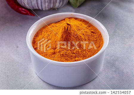 Bright orange spice powder in white ceramic bowl with garlic and red chili in background Bright orange spice powder in white ceramic bowl with garlic and red chili in background 142534057