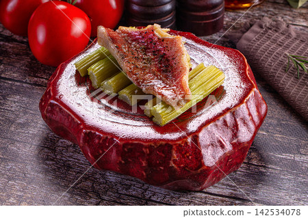 Sea perch fillet on celery stalks served on red ceramic plate with tomatoes and pepper mills Sea perch fillet on celery stalks served on red ceramic plate with tomatoes and pepper mills 142534078