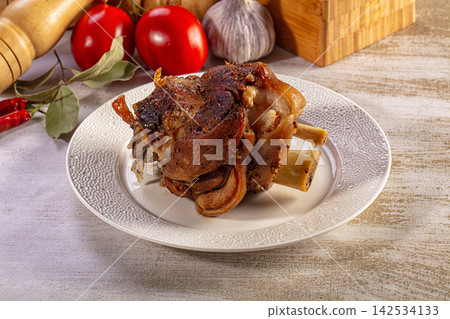 Golden brown roasted pork hock served on a plate with garlic and red tomatoes Golden brown roasted pork hock served on a plate with garlic and red tomatoes 142534133