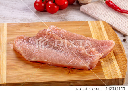 Raw turkey breast slices on wooden cutting board with cherry tomatoes and red chili pepper background Raw turkey breast slices on wooden cutting board with cherry tomatoes and red chili pepper background 142534155