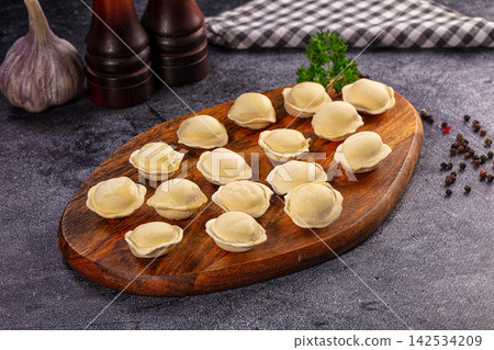 Raw dumplings on wooden cutting board with garlic and peppercorns Raw dumplings on wooden cutting board with garlic and peppercorns 142534209