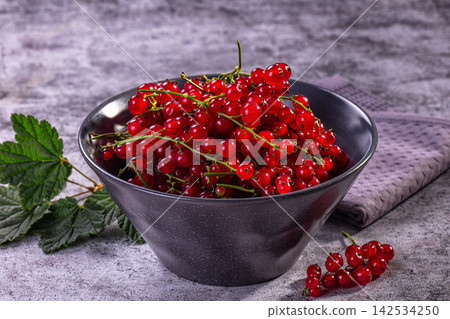 Fresh red currants in black bowl with green leaves on textured gray surface Fresh red currants in black bowl with green leaves on textured gray surface 142534250