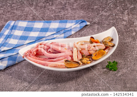 Fresh octopus tentacles and mussels on white plate with blue checkered napkin Fresh octopus tentacles and mussels on white plate with blue checkered napkin 142534341