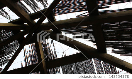 Geometric structure of supporting beams inside a wooden cabin with a reed roof under construction Geometric structure of supporting beams inside a wooden cabin with a reed roof under construction 142534378