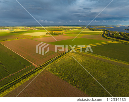 High angle wide horizontal aerial drone photograph of polder fields, drainage canals, Lake Veere, and storm sky in Kamperland, Zeeland, Netherlands in golden hour summer sunlight High angle wide horizontal aerial drone photograph of polder fields, drainage canals, Lake Veere, and storm sky in Kamperland, Zeeland, Netherlands in golden hour summer sunlight 142534383