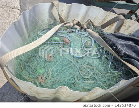 Green mesh fishing net with orange floats stored in a large white bulk bag on the ground Green mesh fishing net with orange floats stored in a large white bulk bag on the ground 142534870