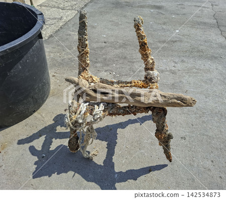 Rusty metal frame with barnacles and sea life supporting driftwood on concrete ground Rusty metal frame with barnacles and sea life supporting driftwood on concrete ground 142534873