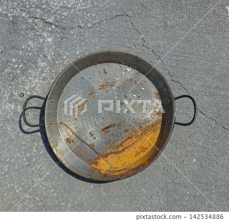 Rusty metal paella pan laying on asphalt surface in a sunny outdoor setting Rusty metal paella pan laying on asphalt surface in a sunny outdoor setting 142534886