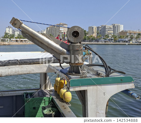 Stainless steel hydraulic crane boom on fishing vessel in harbor with city skyline 142534888
