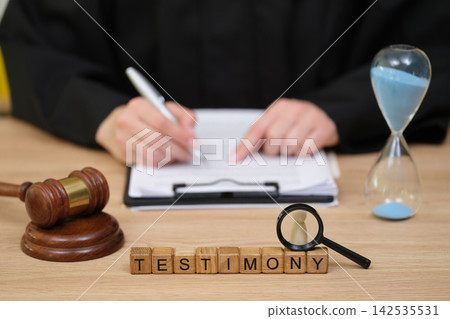 Courtroom testimony in action with focus on a gavel, hourglass, and documents in a legal setting Courtroom testimony in action with focus on a gavel, hourglass, and documents in a legal setting 142535531
