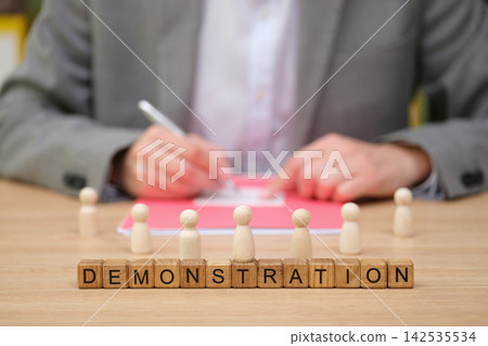 Engaging demonstration with wooden figures and a focused presenter at a table Engaging demonstration with wooden figures and a focused presenter at a table 142535534
