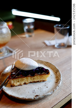 Blueberry tart. A dessert served on a gray plate, with white cream on the side. Blueberry tart. A dessert served on a gray plate, with white cream on the side. 142535596