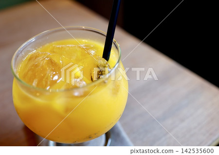 冰鎮柳橙汁。一杯加冰的黃色飲料。附吸管。一張木桌。 142535600