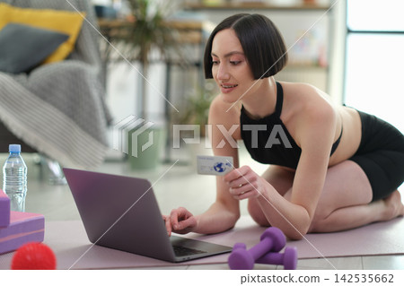 Fit woman makes online payment with bank card after home workout Fit woman makes online payment with bank card after home workout 142535662