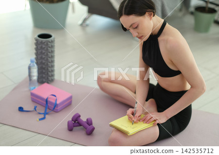 Sporty female sits in relaxed position with pad on training mat Sporty female sits in relaxed position with pad on training mat 142535712