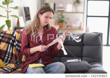 Thoughtful woman reviews collection of detailed shop receipts Thoughtful woman reviews collection of detailed shop receipts 142535801
