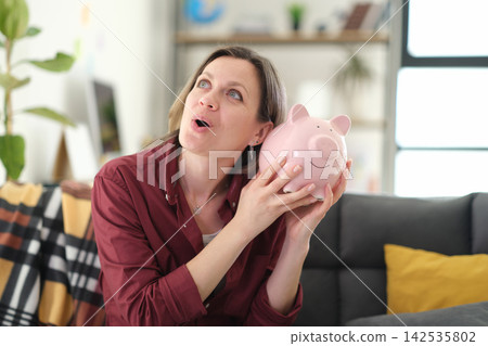 Pleasantly surprised woman shakes charming pig-shaped piggy bank Pleasantly surprised woman shakes charming pig-shaped piggy bank 142535802