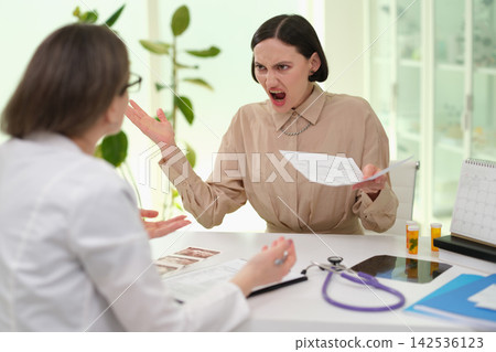 Angry woman arguing with doctor across office desk while holding medical papers in bright clinic interior with stethoscope, test strips, calendar, bottles, and tense consultation mood Angry woman arguing with doctor across office desk while holding medical papers in bright clinic interior with stethoscope, test strips, calendar, bottles, and tense consultation mood 142536123