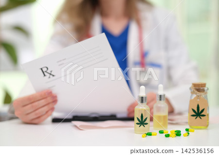 Medical professional holding prescription beside cannabis oil bottles and capsules on desk, suggesting alternative healthcare consultation, pharmacy treatment, wellness guidance, dosage planning Medical professional holding prescription beside cannabis oil bottles and capsules on desk, suggesting alternative healthcare consultation, pharmacy treatment, wellness guidance, dosage planning 142536156
