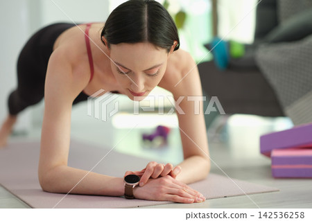Focused woman stands in plank pose and checks heartbeat rate Focused woman stands in plank pose and checks heartbeat rate 142536258