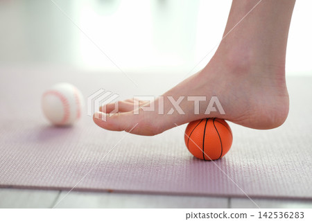 Woman massages bare sole with small ball at home training Woman massages bare sole with small ball at home training 142536283
