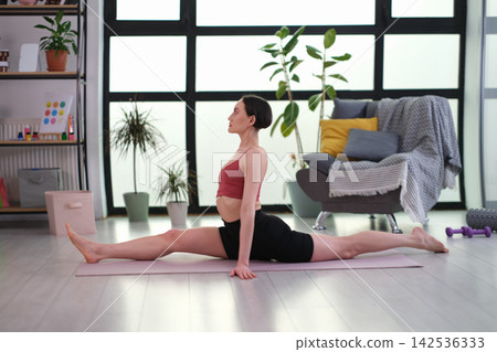 Flexible sportswoman sits in full split on fitness mat Flexible sportswoman sits in full split on fitness mat 142536333