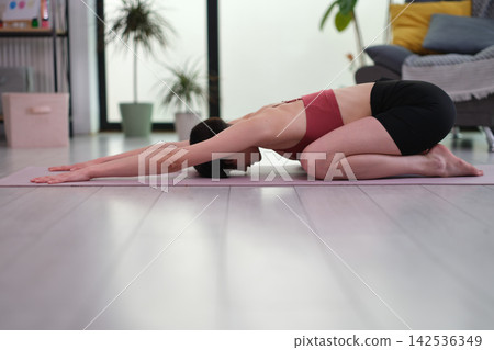 Woman in breathable athletic clothing performs Balasana yoga pose 142536349