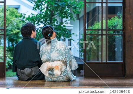 A man and a woman, both dressed in yukata, sit side-by-side on the veranda. A couple enjoying a traditional Japanese summer moment. A man and a woman, both dressed in yukata, sit side-by-side on the veranda. A couple enjoying a traditional Japanese summer moment. 142536468