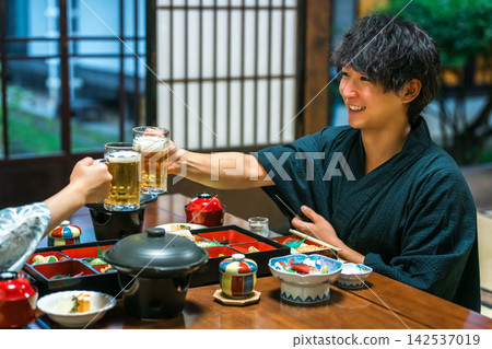 一對身穿浴衣的情侶在溫泉旅館舉杯暢飲啤酒。他們正享受著溫泉之旅和美味的旅館料理。 一對身穿浴衣的情侶在溫泉旅館舉杯暢飲啤酒。他們正享受著溫泉之旅和美味的旅館料理。 142537019