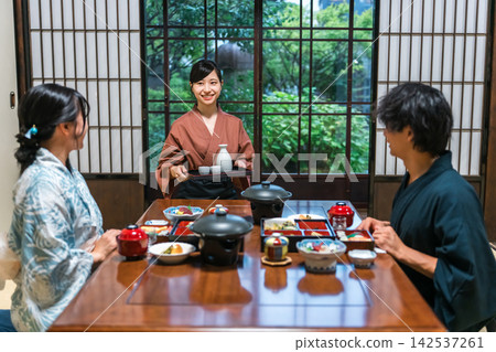 A maid carrying sake at a hot spring inn. Dinner served at the inn, where guests in yukata robes are entertained. A maid carrying sake at a hot spring inn. Dinner served at the inn, where guests in yukata robes are entertained. 142537261