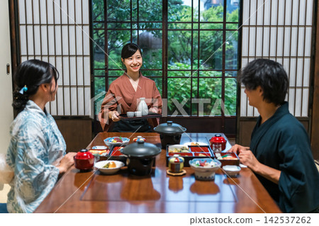 A maid carrying sake at a hot spring inn. Dinner served at the inn, where guests in yukata robes are entertained. A maid carrying sake at a hot spring inn. Dinner served at the inn, where guests in yukata robes are entertained. 142537262