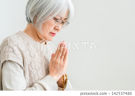 A senior woman prays at the family altar every day, honoring her ancestors at home. A senior woman prays at the family altar every day, honoring her ancestors at home. 142537480