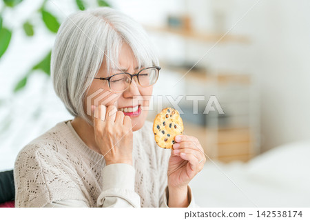 一位老年婦女吃完硬米餅後牙痛。老年人常會遇到咀嚼困難的問題。 一位老年婦女吃完硬米餅後牙痛。老年人常會遇到咀嚼困難的問題。 142538174